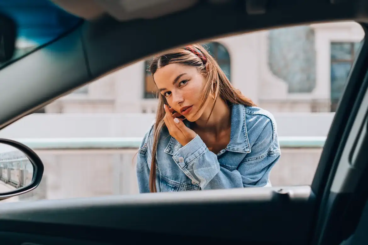 Young woman looking thoughtful through a car window while choosing the right car